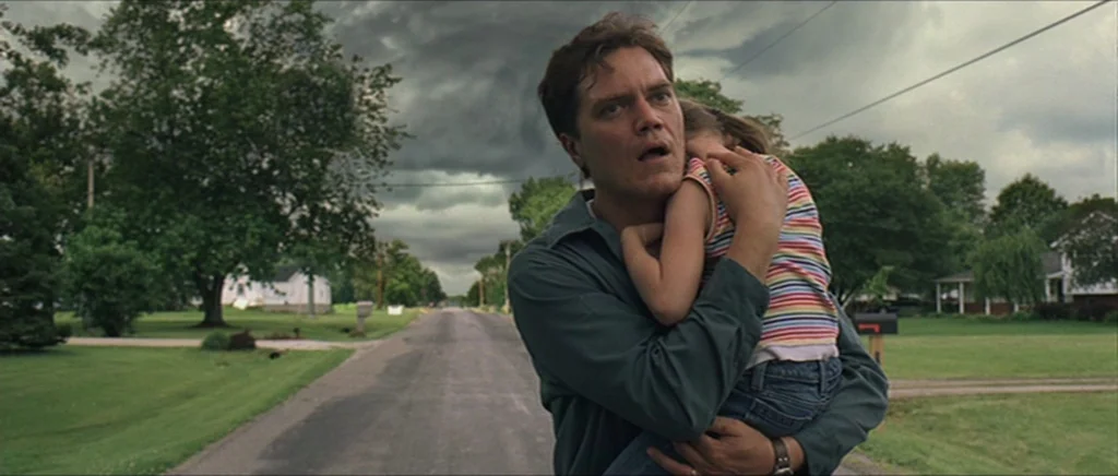 Take Shelter (2011) movie still: medium — A suburban street stretches into the distance beneath dark, heavy, ominous storm clouds. A man stands in…