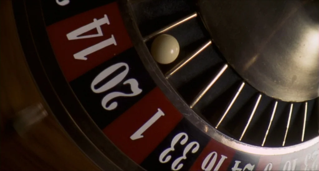 Run Lola Run (1998) movie still: closeup — A polished wooden roulette wheel features black and red numbered pockets under dim lighting. A small…