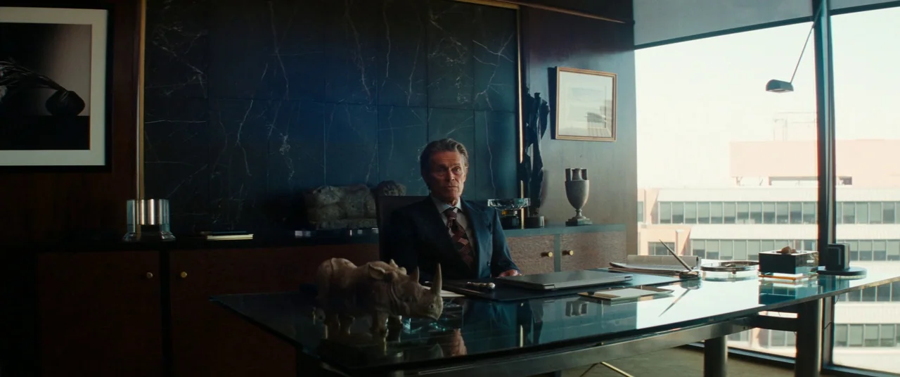 Kinds of Kindness (2024) movie still: medium — An executive suite features a dark marble wall and a glass desk overlooking a cityscape. A…