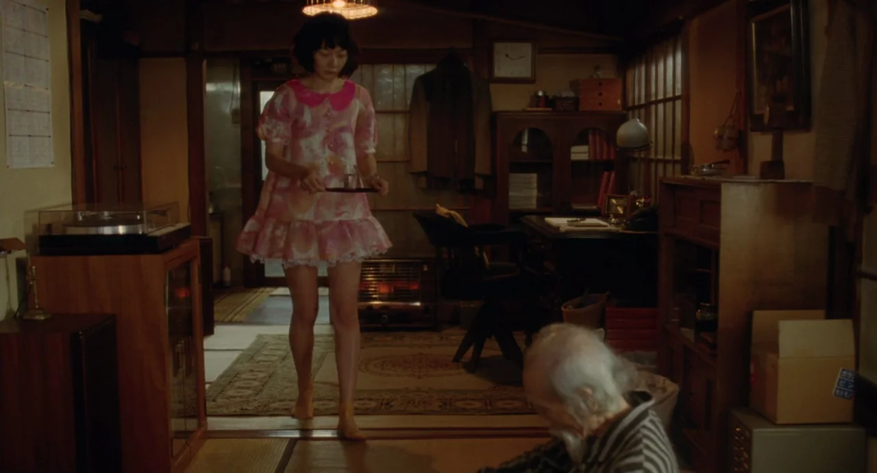 Air Doll (2009) movie still: fullbody — A traditional Japanese room features tatami mats, wood paneling, and an old desk setup. A young woman walks…