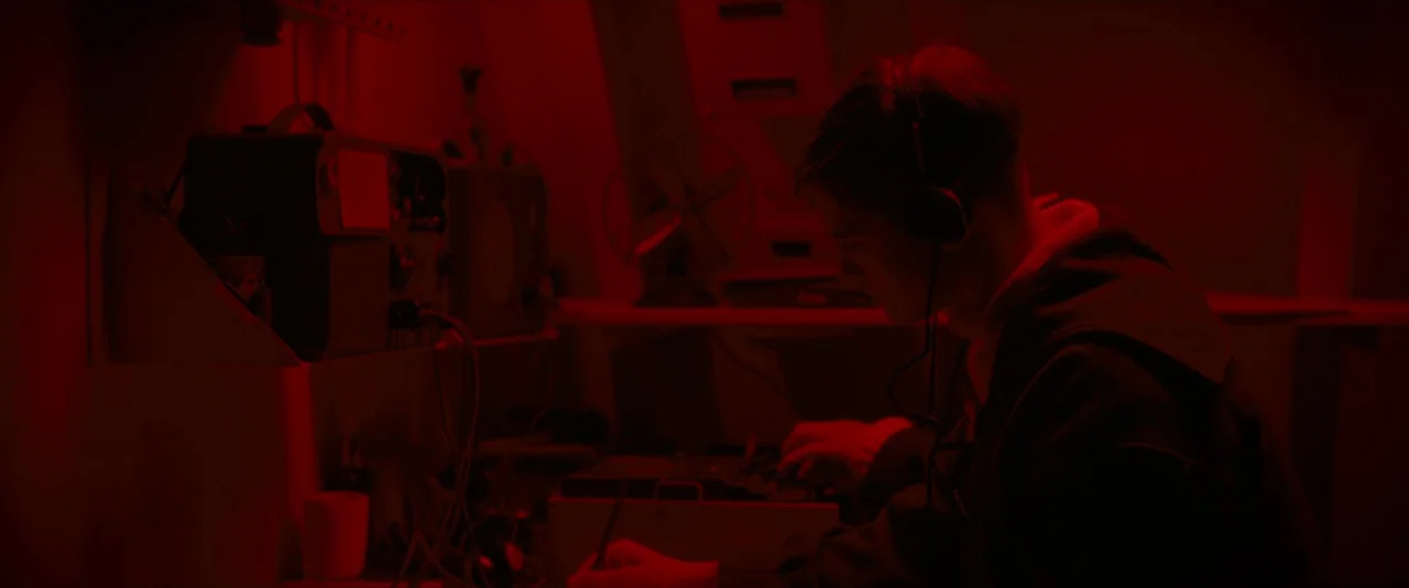 The Imitation Game (2014) movie still: medium — A dark, cramped military workspace is bathed in deep monochromatic red light. A man sits at a desk…