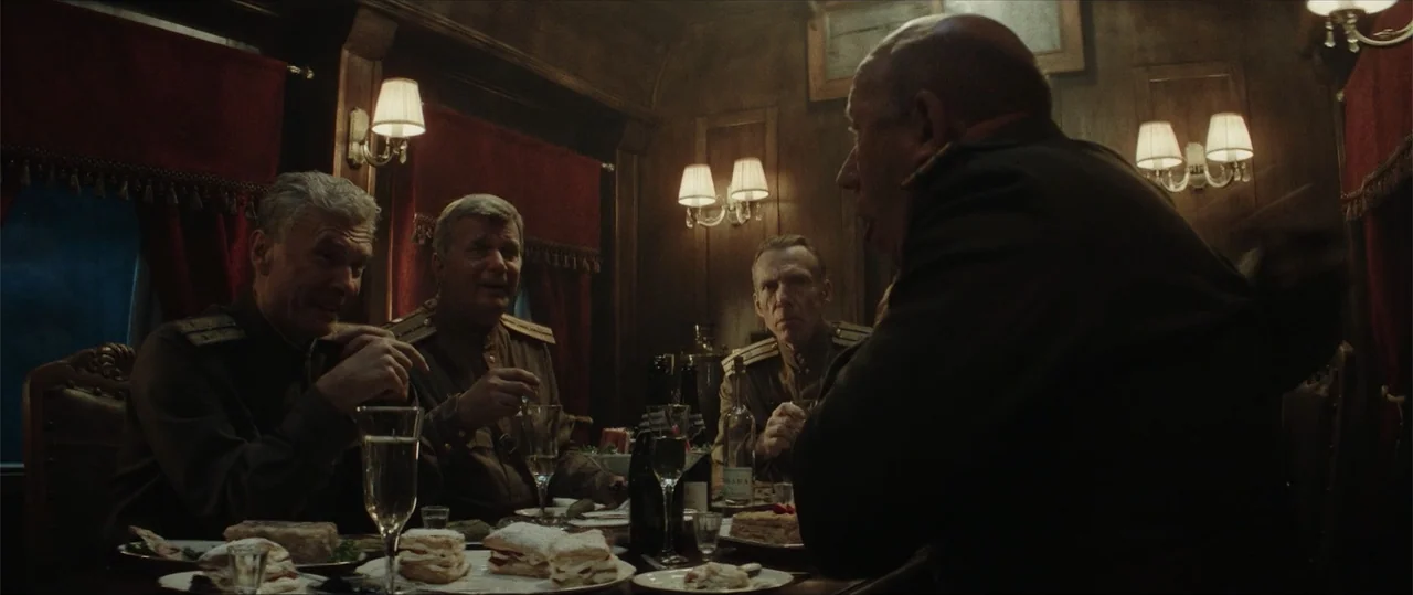 Sisu: Road to Revenge (2025) movie still: medium — A dark wooden train dining car features red velvet curtains and brass light fixtures. Four…