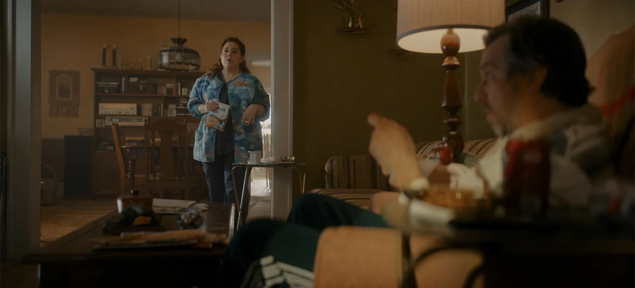 My Best Friend's Exorcism (2022) movie still: medium — A dimly lit residential space features brown walls and a wood shelving unit. A woman holding…