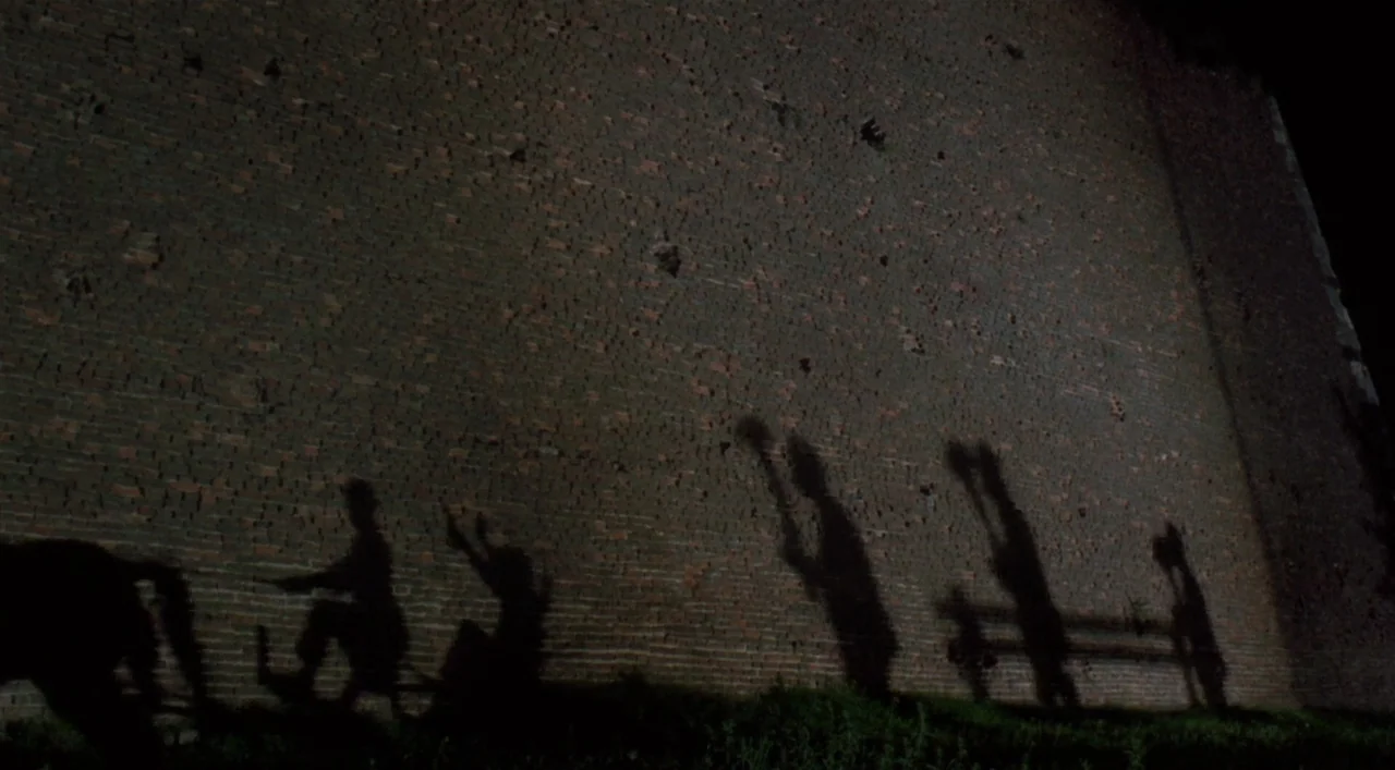 Underground (1995) movie still: wide — A dark, tall brick wall serves as a backdrop for projected silhouettes of figures. The figures are seen in…