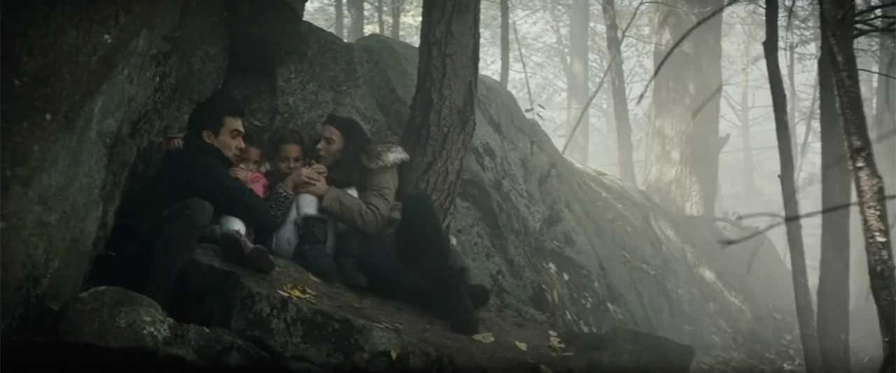 Run All Night (2015) movie still: medium — A group of four huddled people sheltered at the base of large rocks. The subjects are crouching together…