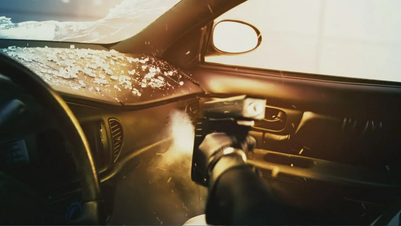 Ultraviolet (2006) movie still: closeup — The interior of a modern car shows a shattered windshield and dusty dashboard. A handgun fires a shot into…