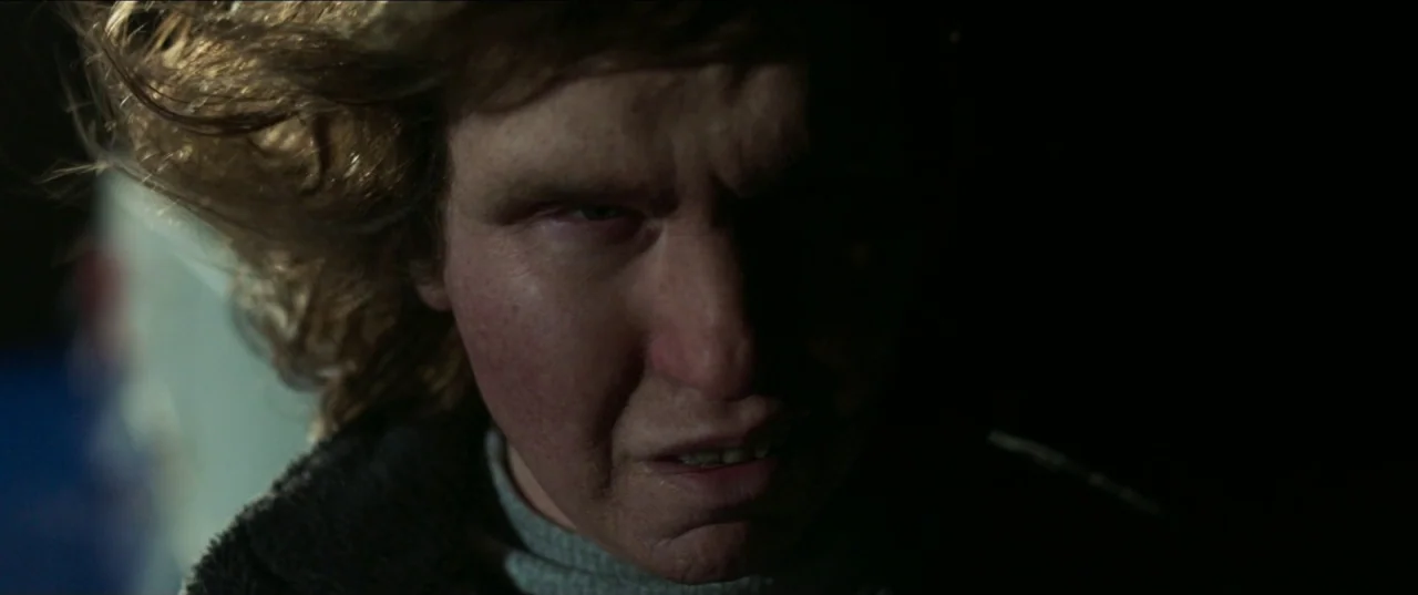 Border movie still: closeup — A dark, shadowed stairwell provides the setting for the close-up portrait of a man. The man stares directly forward…