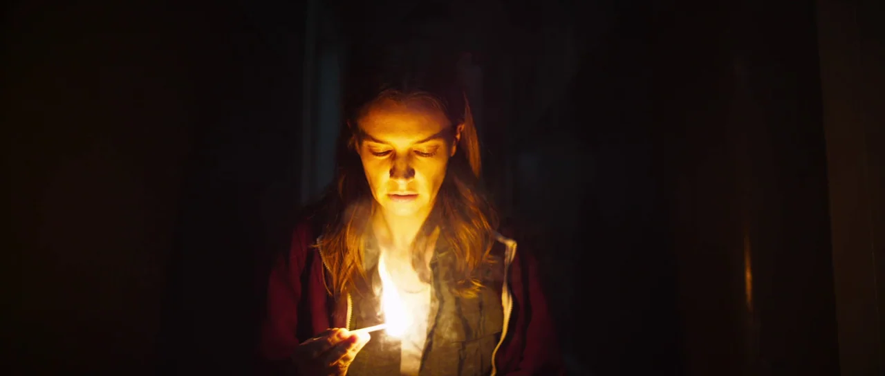 A Dark Song (2016) movie still: medium — A dark, indistinguishable interior space is void of background detail. A young woman holds a single burning…