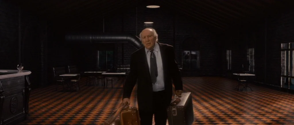 You Ain’t Seen Nothin’ Yet (2012) movie still: fullbody — A dark, expansive hall features a checkered floor and rows of small tables. An elderly man…