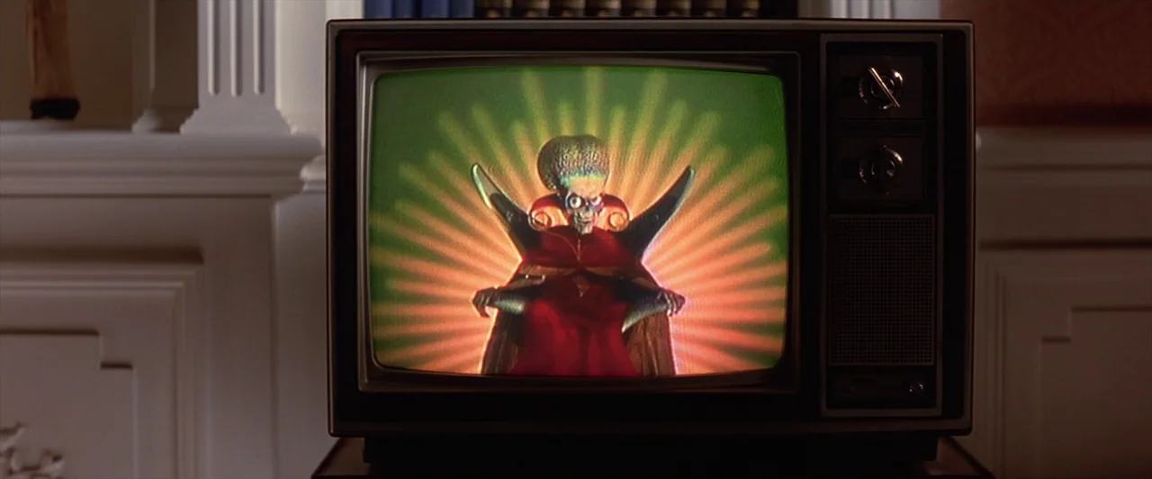 Mars Attacks! (1996) movie still: medium — A vintage television set sits atop a cabinet within a domestic interior. The screen displays an alien…