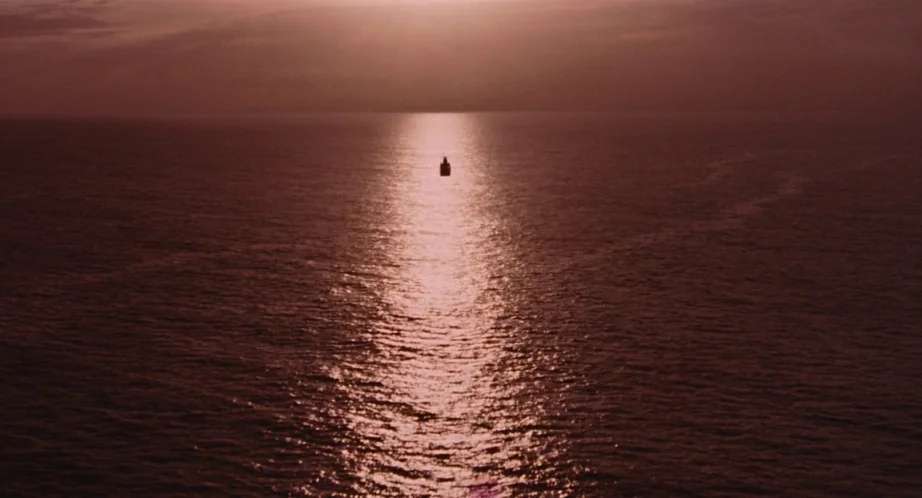 Jurassic Park (1993) movie still: establishing — A vast expanse of ocean is illuminated by the light of a setting sun. A lone small boat floats in…