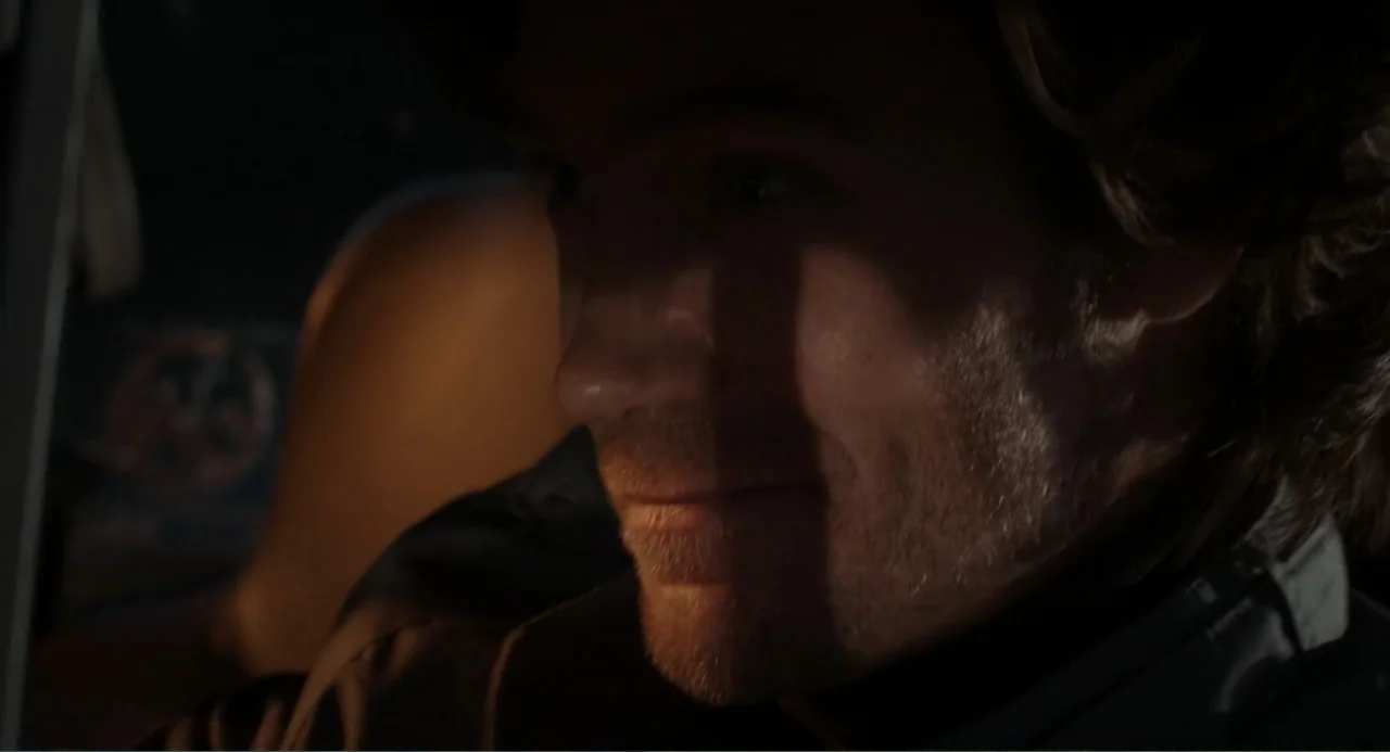 Ted Bundy: American Boogeyman (2021) movie still: closeup — The interior of a vehicle at night with warm light illuminating the driver. A man with…