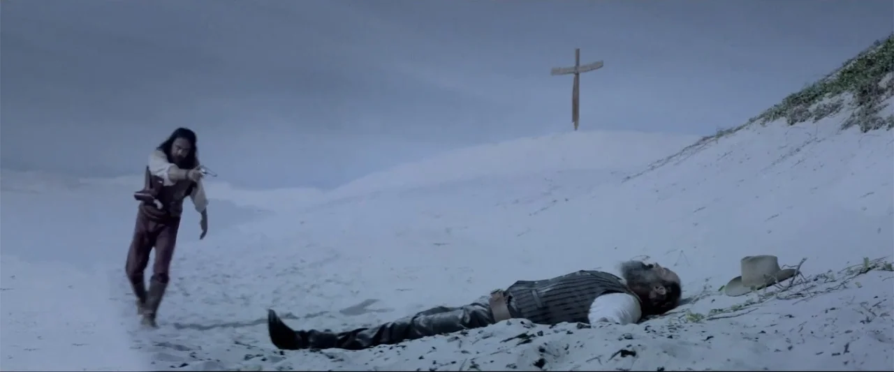 Matar o morir (1984) movie still: wide — A vast expanse of white sand dunes features a lone wooden cross on a hill. A man stands holding a firearm…