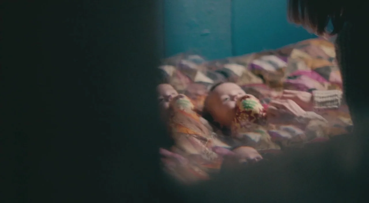 Broken (2012) movie still: medium — A dimly lit room features a patterned quilt on a flat surface. A woman reaches out toward two small infants…