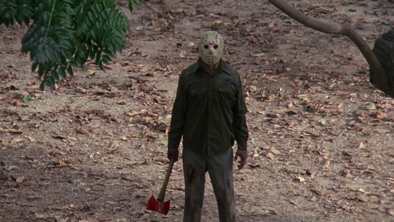 Friday the 13th: A New Beginning (1985) movie still: fullbody — A forest floor is covered in thick layers of brown dead leaves. A masked figure…