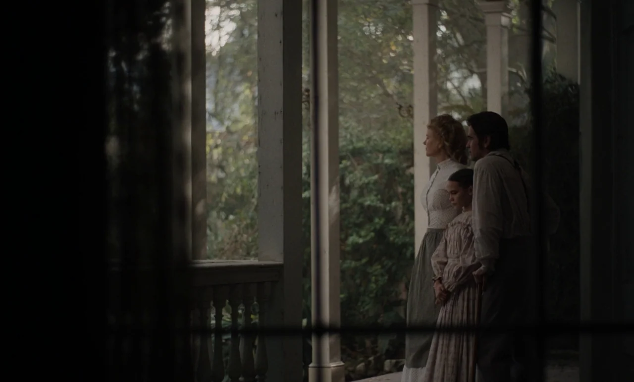The Beguiled (2017) (2017) movie still: medium — A wooden porch with white columns overlooks dense foliage in the background. A man, woman, and…