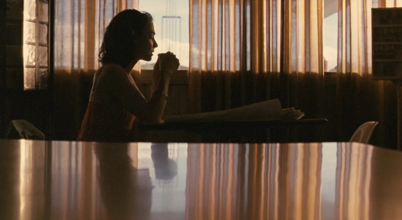 Patagonia (2010) movie still: medium — A diner booth interior is illuminated by sunlight streaming through thin window curtains. A woman sits in…