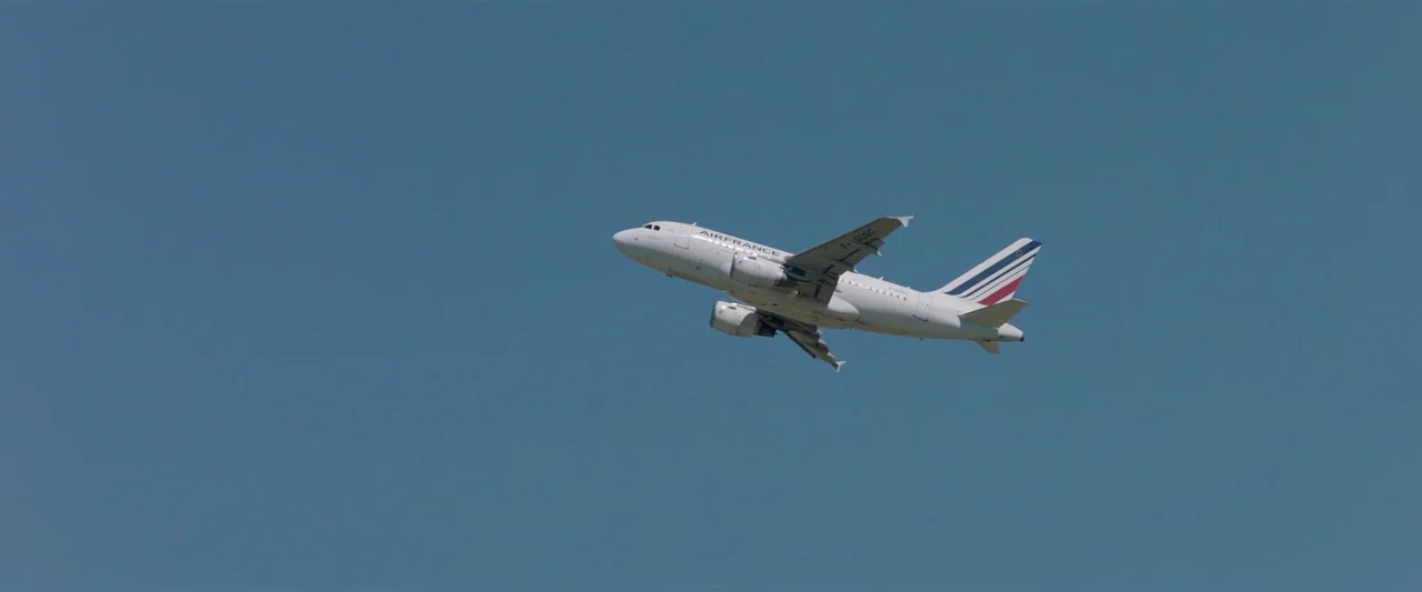 Sibyl (2019) movie still: wide — A white Air France passenger jet climbs into a vast, cloudless blue sky. The aircraft is captured in profile…