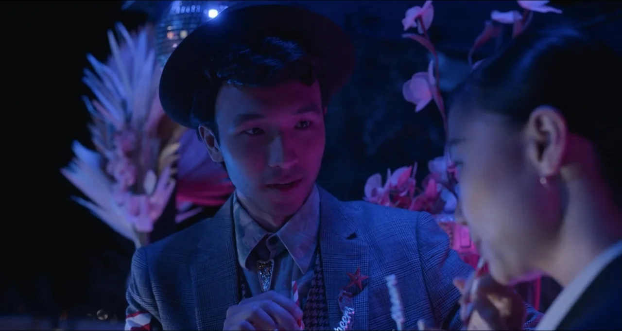 Five Blind Dates (2024) movie still: medium — A night party setting features an East Asian man wearing a hat and blazer. He stands near a woman…