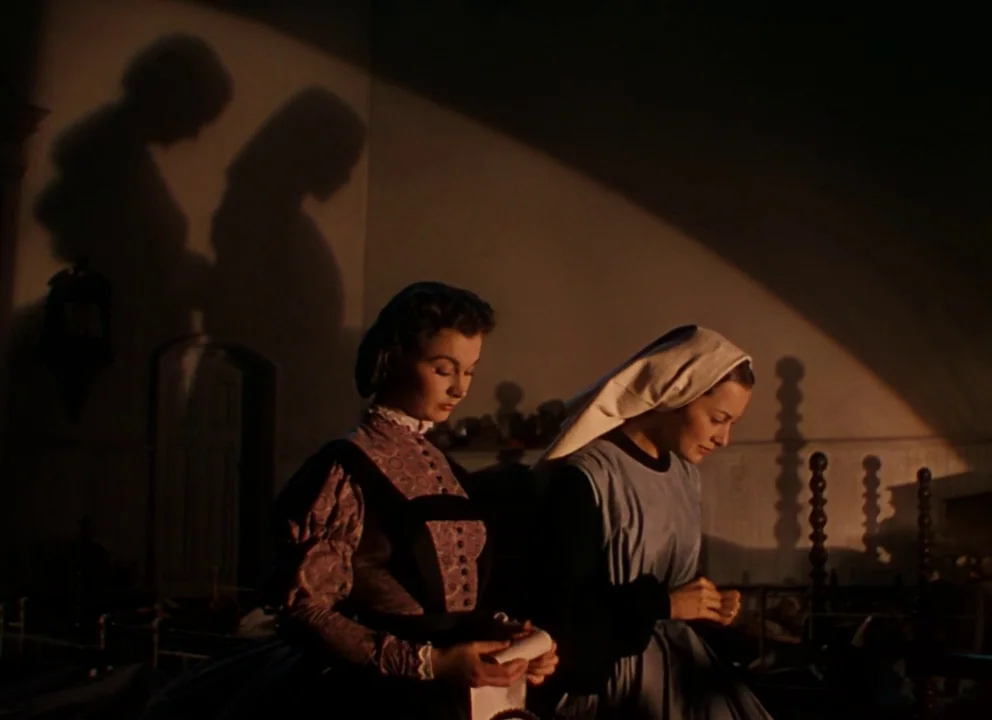 Gone with the Wind (1939) movie still: medium — Two women stand in a dimly lit nursery with antique furniture casting shadows behind them. One woman…