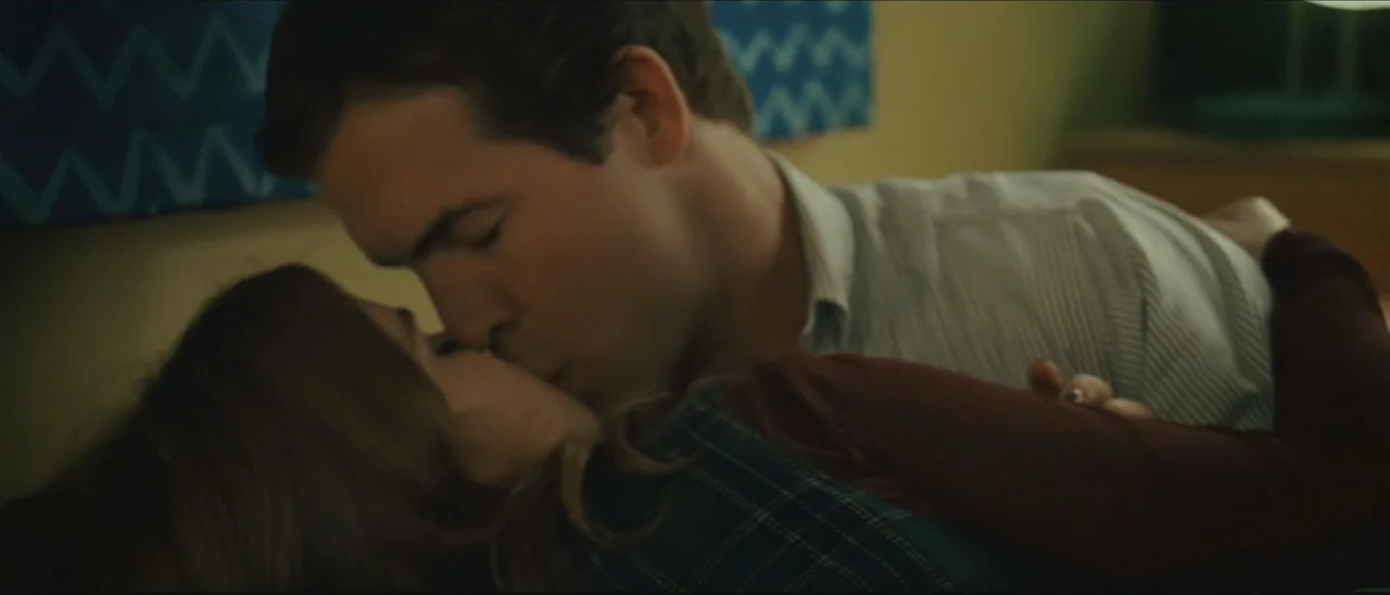 Definitely, Maybe (2008) movie still: closeup — A dimly lit room with muted walls featuring abstract chevron pattern decor. A man and a woman kiss…
