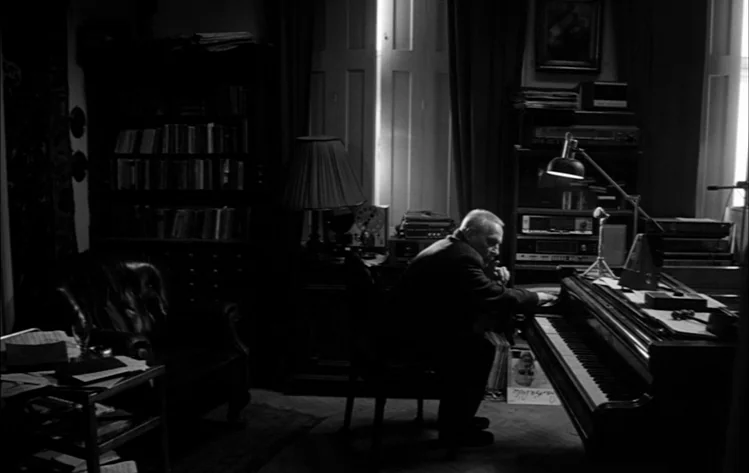 Werckmeister Harmonies (2000) movie still: medium — A cluttered room features a piano, bookshelves, and various electronic recording equipment. An…