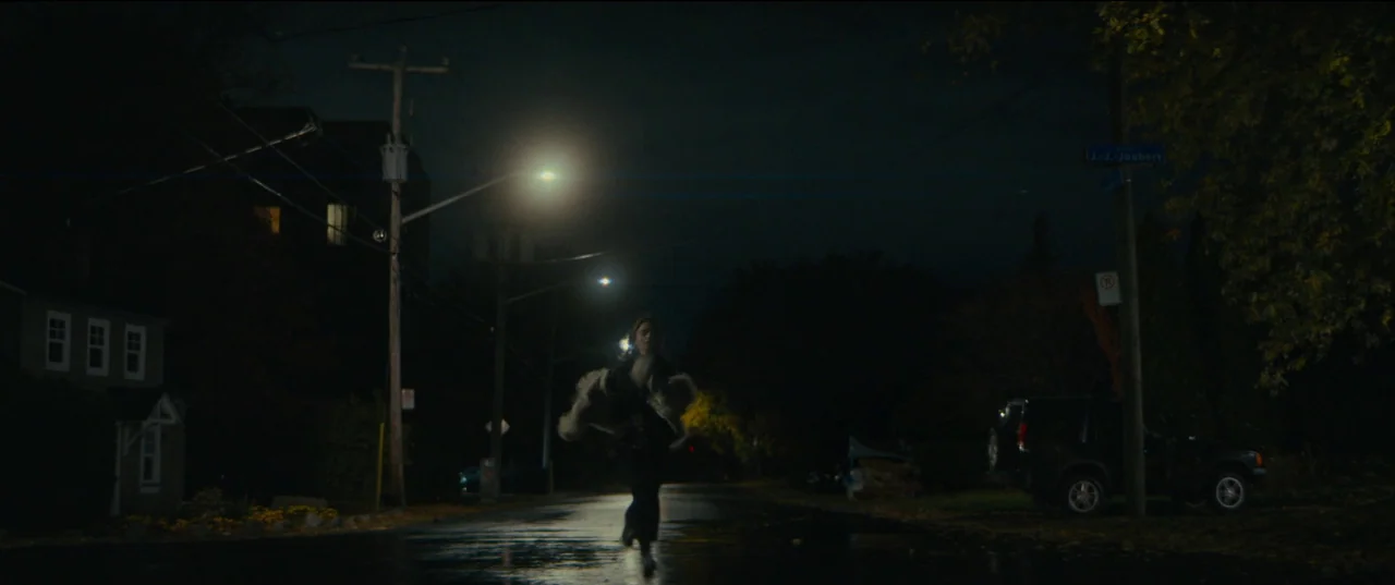 Humanist Vampire Seeking Consenting Suicidal Person (2023) movie still: wide — A dark residential street at night is illuminated by tall overhead…