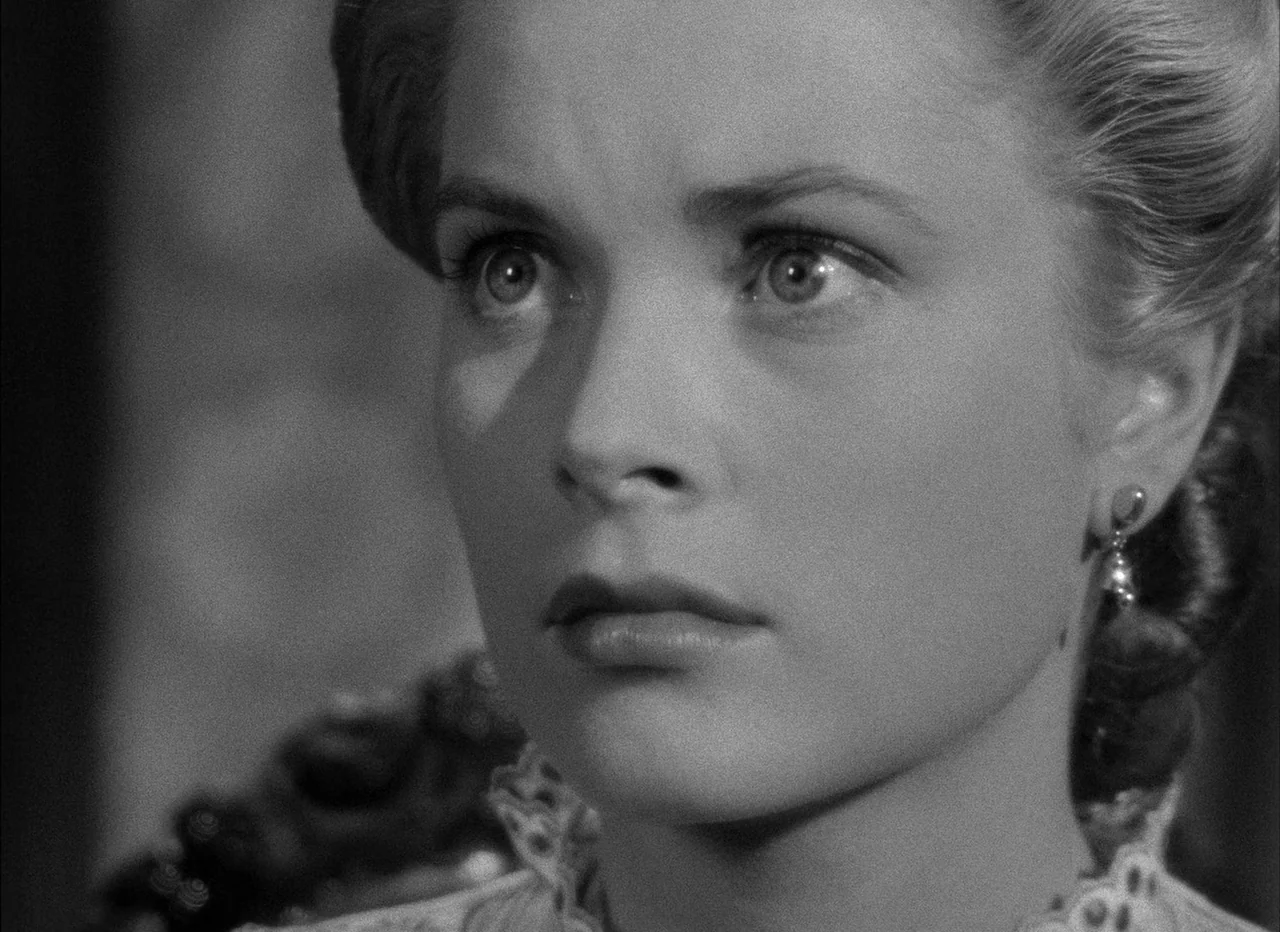 High Noon (1952) movie still: closeup — A close-up view of a woman indoors against a blurred background. She turns her head slightly while gazing…