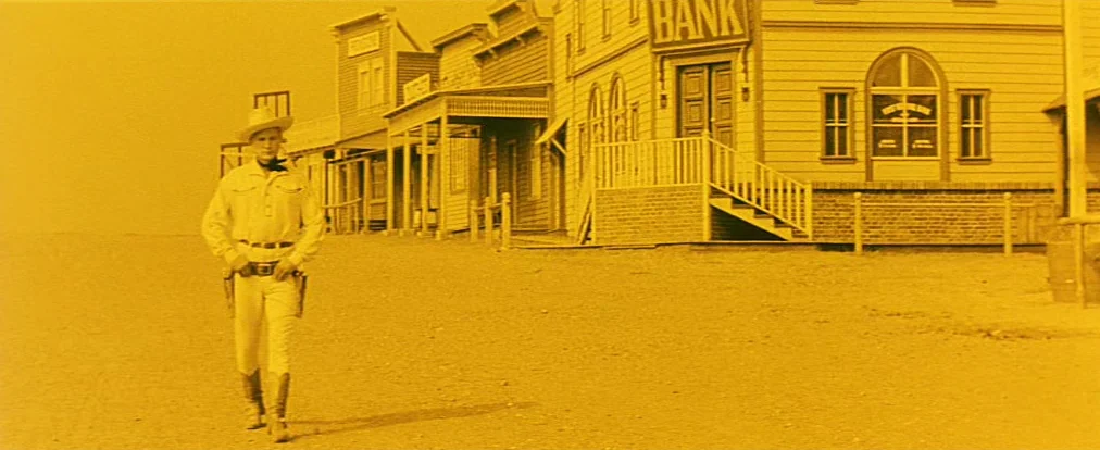 Lemonade Joe (1964) movie still: fullbody — A wooden main street of an American Old West town features a bank building. A solitary man in western…
