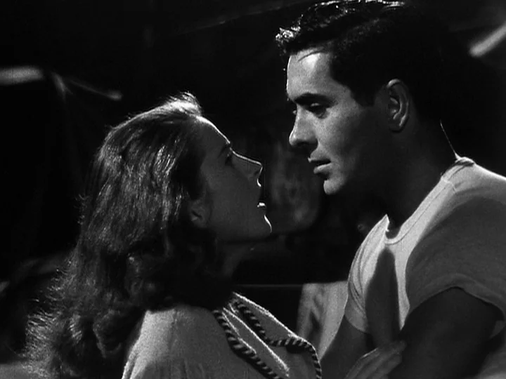 Nightmare Alley (1947) movie still: medium — An interior space is dimly lit by a strong, singular directional light source. A young man and woman…