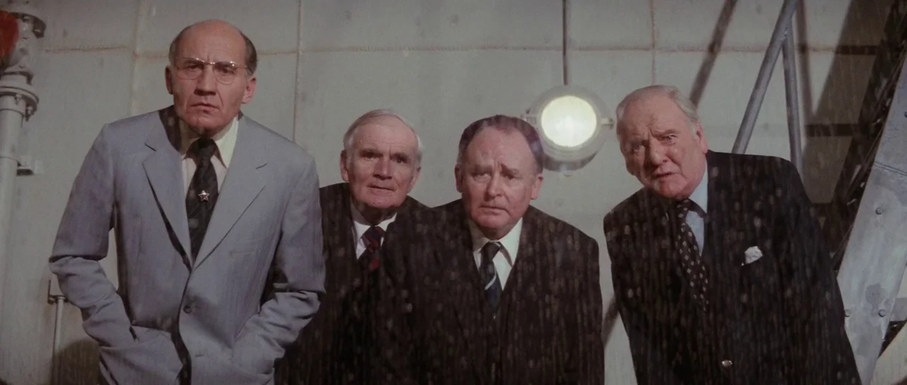 The Spy Who Loved Me (1977) movie still: medium — A stark industrial space featuring light gray concrete walls and a circular bulkhead light. Four…
