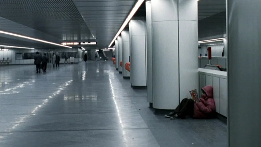 71 Fragments of a Chronology of Chance (1994) movie still: wide — A modern, minimalist transit terminal features long rows of grey columns and…