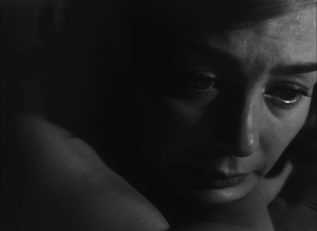 Hiroshima Mon Amour (1959) movie still: closeup — A dark, minimally lit interior space creates a high-contrast focus on a person. The subject rests…