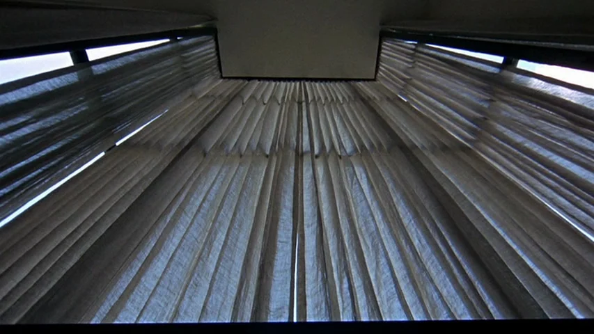 Petulia (1968) movie still: establishing — Floor to ceiling thin fabric curtains hang across a windowed wall. The curtains are pulled closed in the…