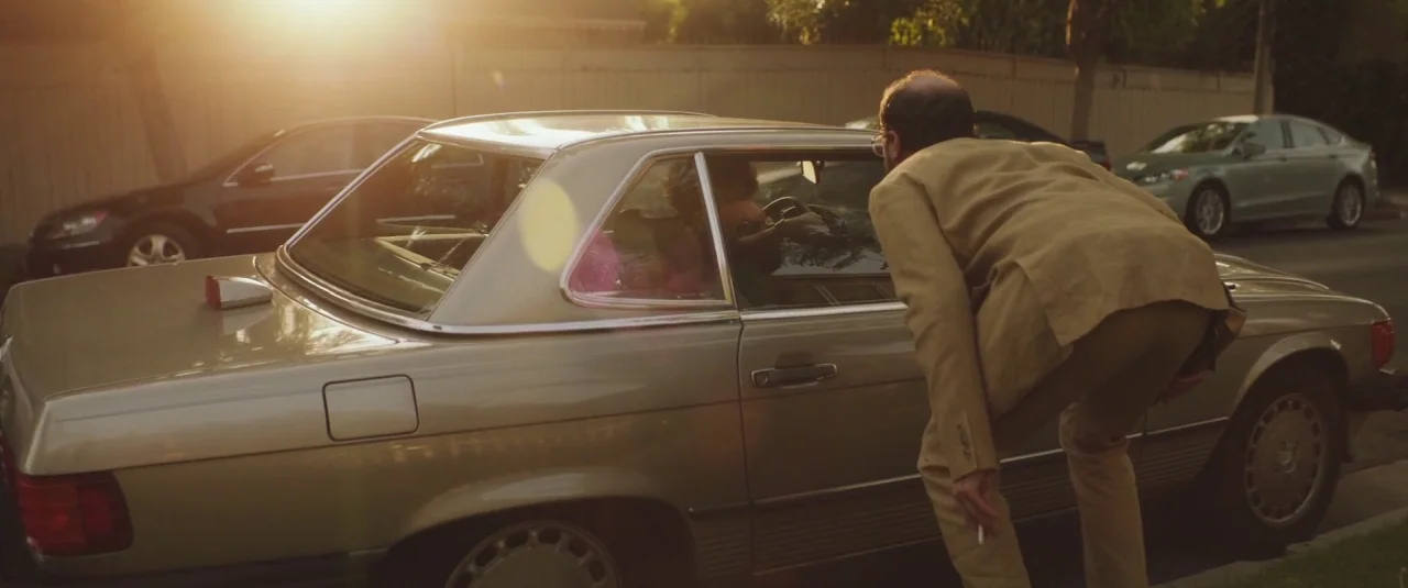 Lemon (2017) movie still: medium — A man in a tan suit leans down beside a metallic silver Mercedes-Benz coupe. The setting is a residential city…