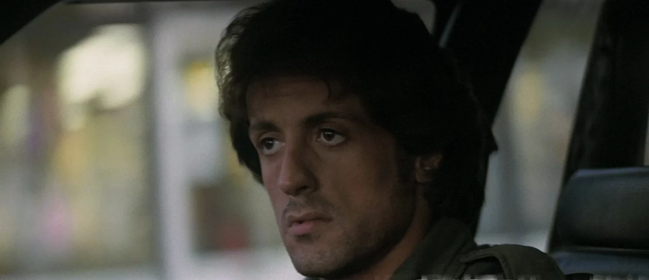 First Blood (1982) movie still: closeup — The interior of a vehicle shows a man sitting in the driver's seat. He gazes towards the side window of…