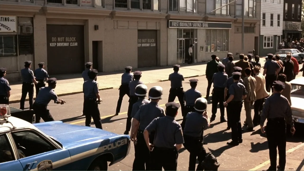 Dog Day Afternoon (1975) movie still: wide — A city street in front of a brick bank building during daytime hours. Multiple police officers in…