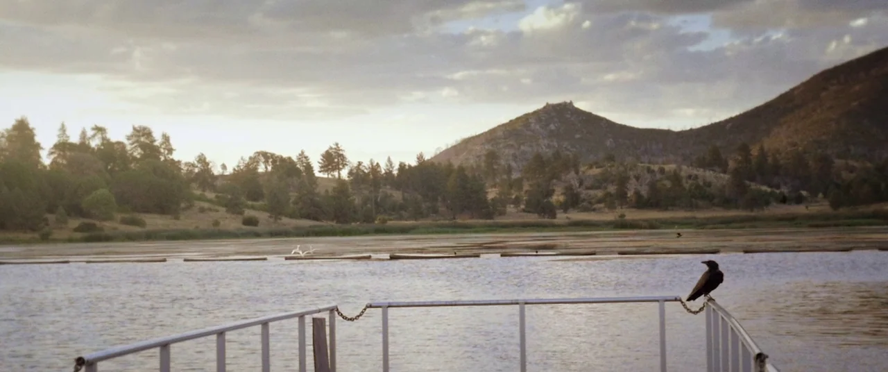 The Endless (2017) movie still: wide — A metal dock extends into a still, expansive lake surrounded by rolling hills and trees. A solitary black…