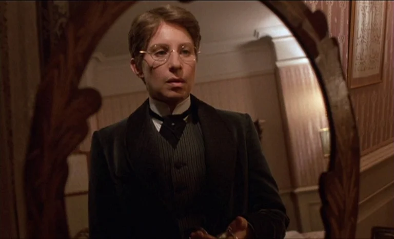 Yentl (1983) movie still: medium — A dimly lit room with ornate wallpaper is reflected in a wooden-framed oval mirror. A person in formal period…