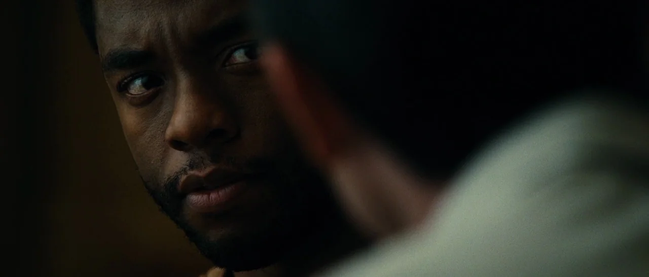 Message From The King (2016) movie still: closeup — A dark, dimly lit indoor setting with soft lighting on a man's face. The man gazes toward an…