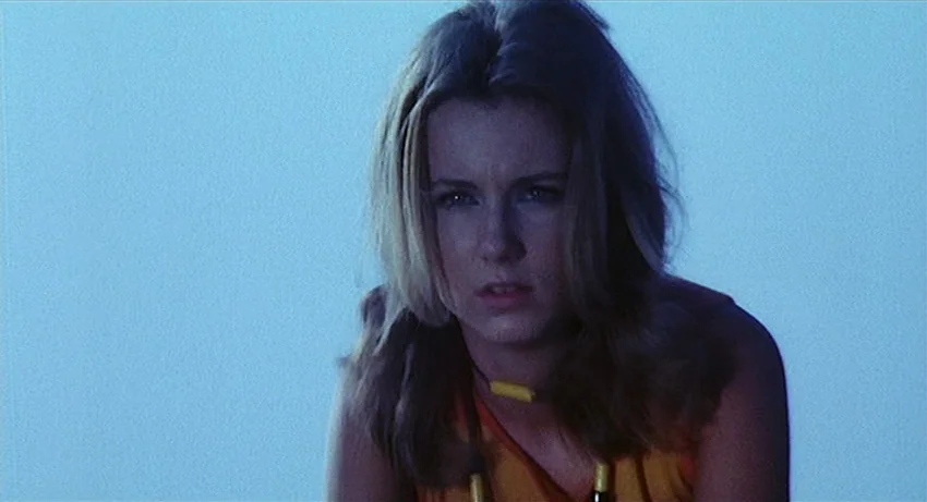 5 Dolls for an August Moon (1970) movie still: medium — A woman stands against a solid blue background that fills the entire frame. The subject is…