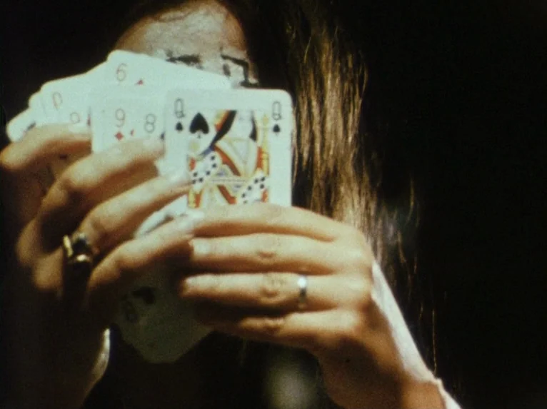 Our Lady of the Turks (1968) movie still: closeup — A dark, dimly lit indoor setting focuses on a person holding cards. The subject covers their…