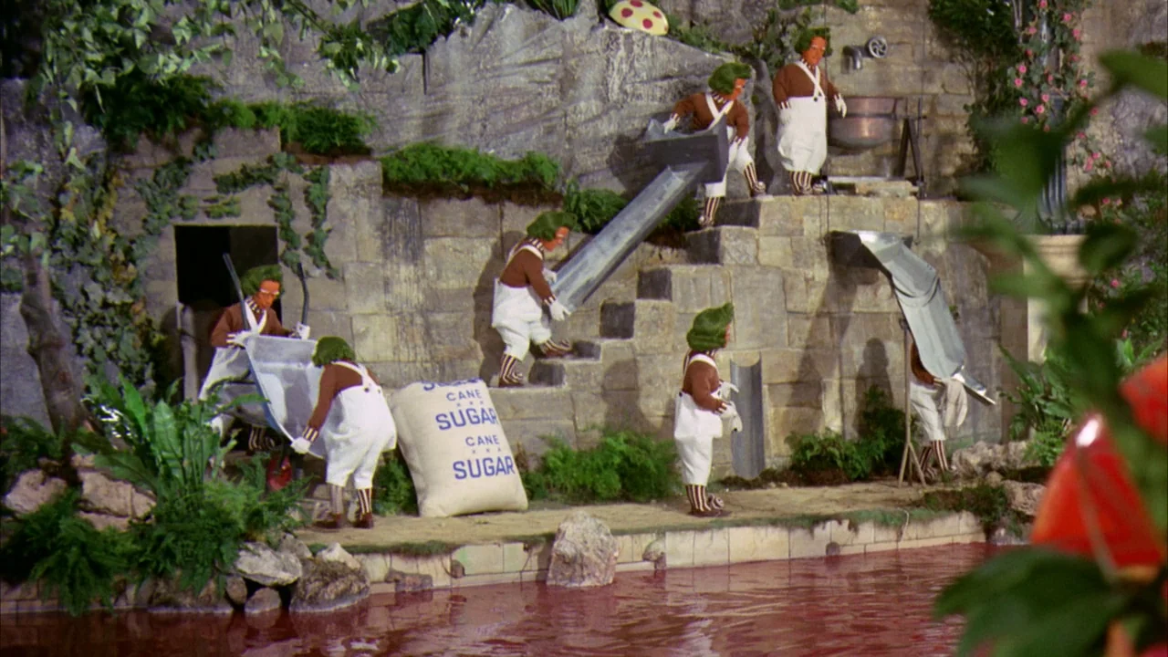 Willy Wonka & the Chocolate Factory (1971) movie still: wide — A stone-walled factory exterior features a bubbling red river and industrial chutes.…