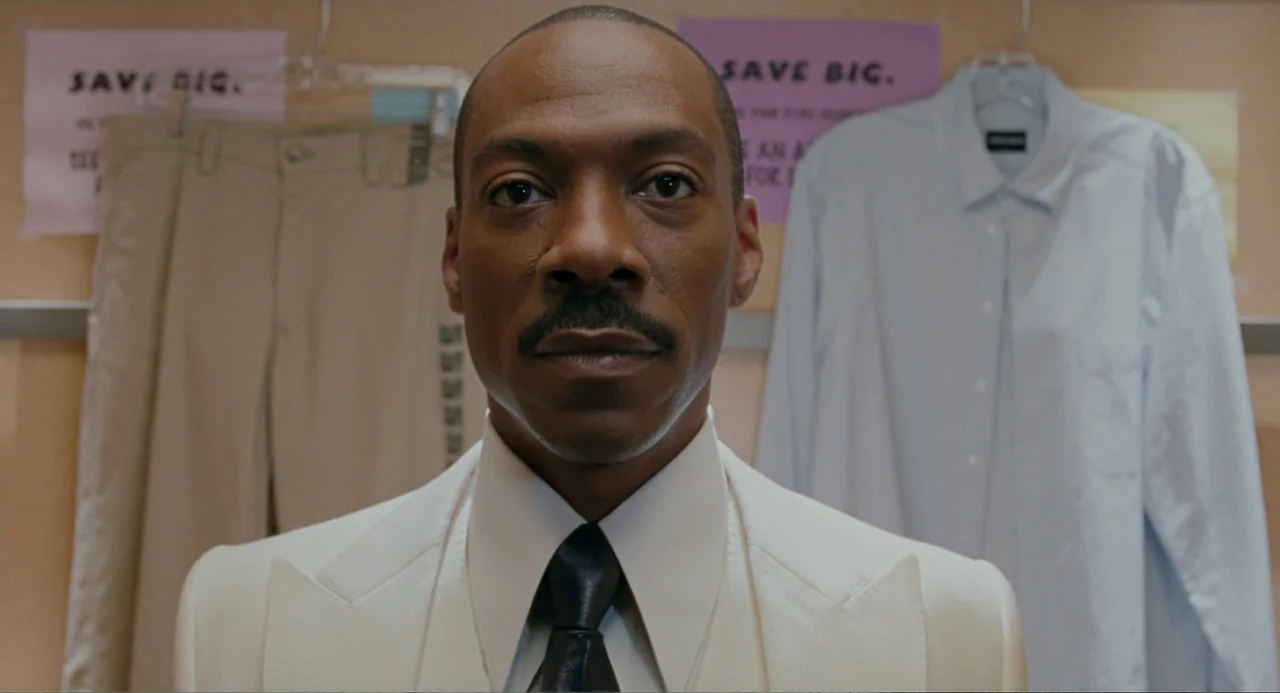 Meet Dave (2008) movie still: closeup — A retail display wall features hung tan trousers and a blue dress shirt. A man stands in the center…