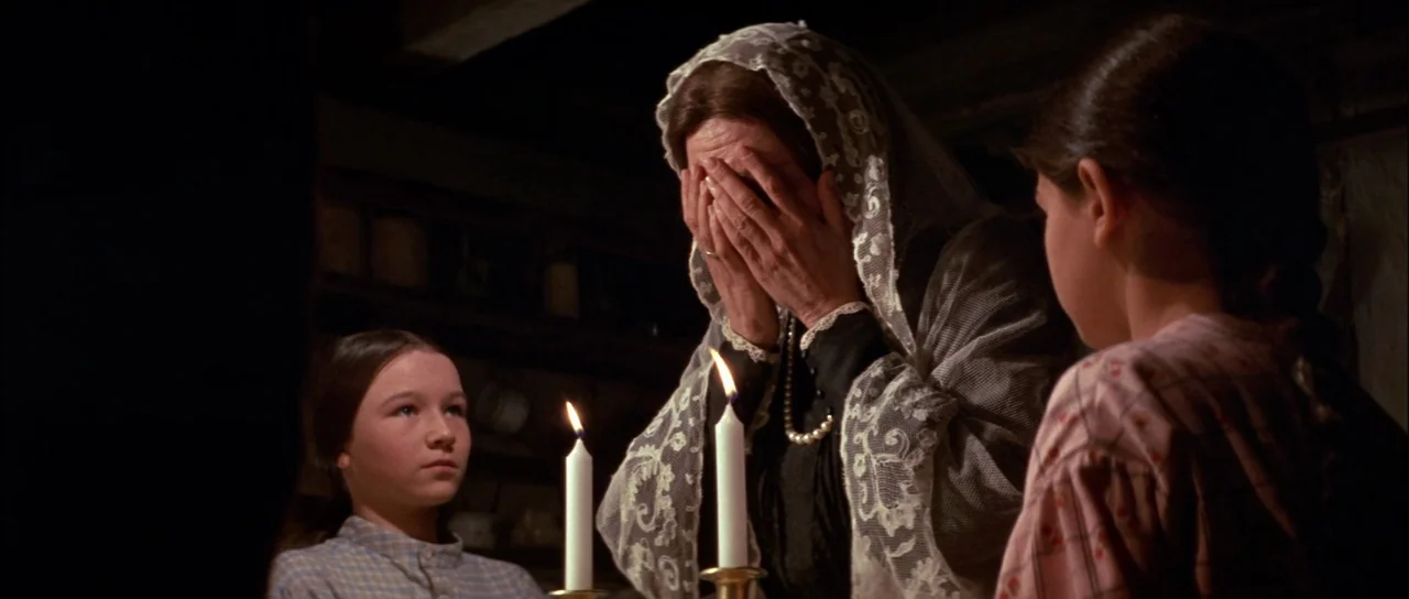 Fiddler On The Roof (1971) movie still: medium — A dimly lit room contains three people gathered around a wooden table at night. An older woman in a…