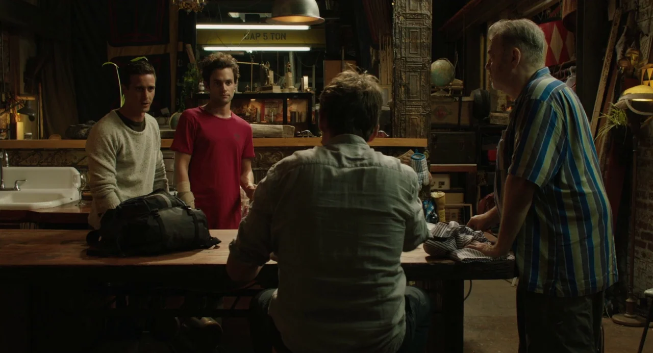 Cymbeline (2014) movie still: medium — A cluttered industrial workspace featuring various tools and objects resting on shelves. Three men stand near…