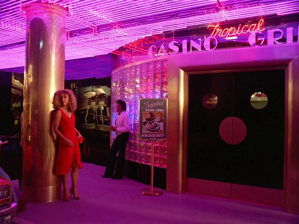 One From The Heart (1982) movie still: fullbody — A casino entrance features a gold-trimmed door and a wall of translucent glass blocks. A woman in…