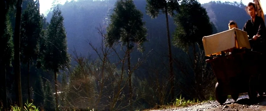 Lone Wolf and Cub: Sword of Vengeance (1972) movie still: wide — A rural mountain path bordered by tall evergreen trees stands in the background. A…