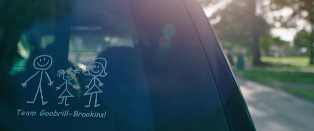 Keanu (2016) movie still: closeup — A close-up of a rear car window with a white stick figure family decal. The sticker includes the text Team…
