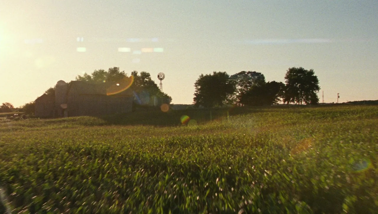 Justice League (2017) movie still: establishing — A rural cornfield extends toward a weathered wooden barn and a metal windmill. The late afternoon…
